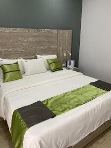 Una gran cama blanca con almohadas verdes. en Bano Palace Hotel, en Douala