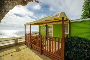 a green house with a wooden deck next to the ocean at Alannia Costa Dorada in Platja de l’Almadrava