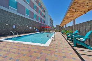 a swimming pool with two blue chairs next to a building at Home2 Suites Corpus Christi Southeast, Tx in Corpus Christi