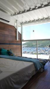 ein großes Bett in einem Zimmer mit einem großen Fenster in der Unterkunft Suit's Bella Vista Arraial do Cabo in Arraial do Cabo