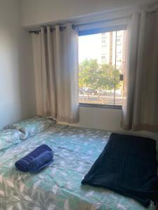 a bed with a blue pillow on it in front of a window at Apto 2 qts, wifi, netflix, metrô próximo in Brasília