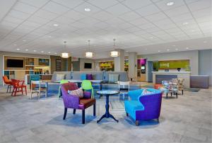 Home2 Suites by Hilton Fort Myers Colonial Blvd في فورت مايرز: لوبى مع كراسي ملونة وطاولات في مكتبة