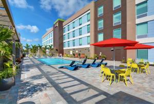 邁爾斯堡的住宿－Home2 Suites by Hilton Fort Myers Colonial Blvd，一个带桌椅和红色遮阳伞的游泳池