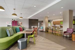 eine Lobby mit einer grünen Couch sowie Tischen und Stühlen in der Unterkunft Home2 Suites By Hilton Martinsburg, Wv in Martinsburg