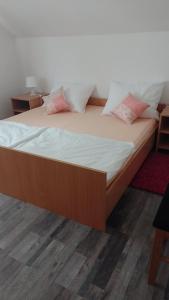 Cama grande de madera con sábanas blancas y almohadas rosas en KETI, en Plaški