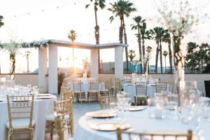 レドンドビーチにあるRedondo Beach Hotel, Tapestry Collection by Hiltonの白いテーブルと椅子、ヤシの木が並ぶ結婚式のレセプション