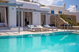 a swimming pool with chairs and a villa at Terra White Seaview Pool Apartments & Suites in Mikonos