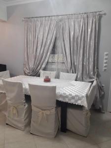 une table blanche avec des chaises et une fenêtre avec des rideaux dans l'établissement Deluxe Sophia`s Penthouse Apartment, à Karpathos
