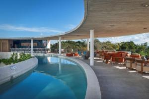 una piscina con mesas y sillas junto a un edificio en Hilton Garden Inn Cancun Airport en Cancún