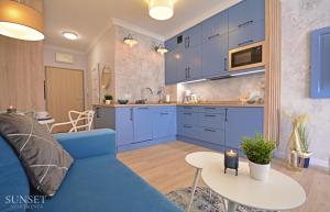 a kitchen and living room with blue cabinets and a blue couch at Sunset Apartments - Kormoran - Plaża 300m - Parking automatyczny in Świnoujście