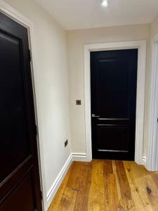 una stanza vuota con due porte nere e pavimenti in legno di Modern 1bedflat Kensington a Londra