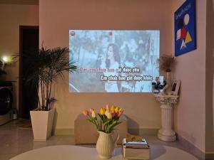 a projection screen in a room with a table with flowers at MADLAD SPACE homestay in Kinh Dinh