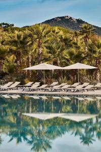 una piscina con sillas, sombrillas y palmeras en Les Prairies de la Mer, en Grimaud