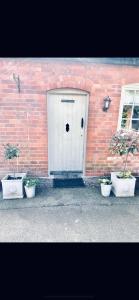 a white door with three potted plants in front of a brick building at STABLE COTTAGE in Cheswardine
