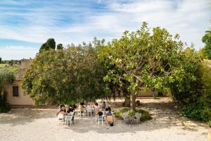 Farm stay La Frescura Agriturismo في سيراكوزا: مجموعة من الناس يجلسون على الطاولات تحت شجرة