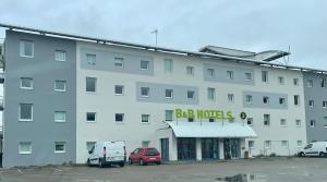 un gran edificio blanco con coches aparcados en un aparcamiento en B&B HOTEL Calais Terminal Cité Europe 2 étoiles, en Coquelles