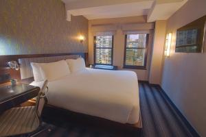 a bedroom with a bed and a desk and two windows at Hotel Edison Times Square in New York
