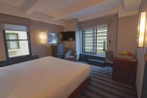 a bedroom with a bed and a desk and two windows at Hotel Edison Times Square in New York