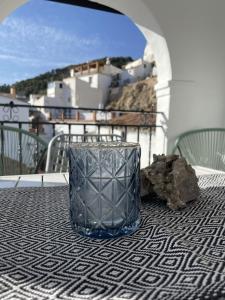 Olive & Ivy Guesthouse في Canillas de Aceituno: وجود مزهرية زجاجية على طاولة في الشرفة