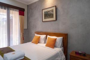 1 dormitorio con 1 cama con sábanas blancas y almohadas de color naranja en Kubu Indah Homestay Sanur en Sanur