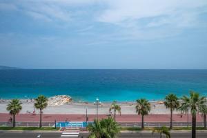 Blick auf einen Strand mit Palmen und das Meer in der Unterkunft Le balcon de la baie des Anges in Nizza