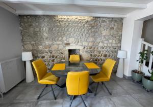 a dining room with yellow chairs and a stone wall at Petite'Escale in Charmes-sur-Rhône