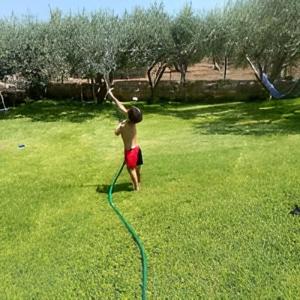 a boy in a yard with a water hose at Nasia’s house in Kineta