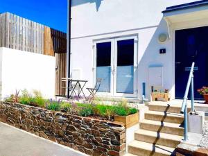 a white house with a stone wall and stairs at Modern chic summer holiday retreat. in Newquay
