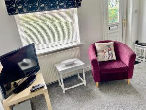 a living room with a purple chair and a tv at Bluebell Cottage in Selby