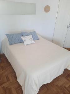 a white bed with blue pillows on top of it at Mar de Anto in Puerto Madryn