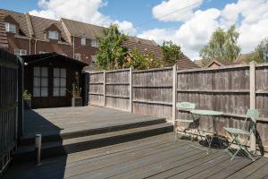 a wooden deck with chairs and a fence at Large 4 Bed Ideal for Contractors - Free Parking in Bedford