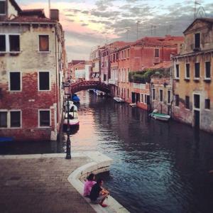 dos personas sentadas en una cornisa junto a un canal en Venice Romantic Home, en Venecia