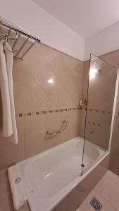 uma casa de banho com uma banheira e um chuveiro com uma porta de vidro em Hotel Del Comahue em Neuquén