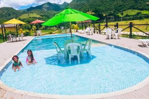 two children playing in a swimming pool with a green umbrella at Pousada Sítio da Floresta in Sana