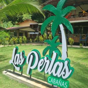 un panneau devant un complexe avec un palmier dans l'établissement Cabañas las perlas, à Bahía Solano