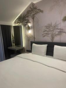 Uzunkum Hotel في طرابزون: غرفة نوم مع سرير أبيض كبير مع أشجار النخيل على الحائط