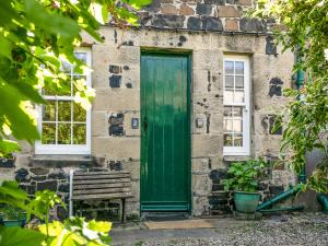 een groene deur op een stenen gebouw met een bank bij Elliot Cottage in Bamburgh