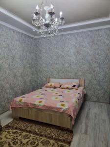 1 dormitorio con cama rosa y lámpara de araña en Deluxe, en Shymkent