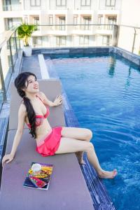 une femme en bikini rouge assise à côté d'une piscine dans l'établissement Sea Wind Hotel by THG, à Đà Nẵng