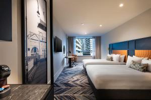 a hotel room with two beds and a desk at Dorsett Melbourne in Melbourne