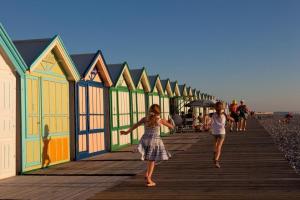 dos chicas caminando por un paseo marítimo con cabañas de playa en l'albatros "le pont", en Cayeux-sur-Mer