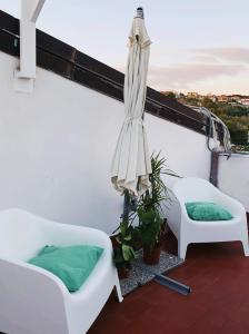 un balcón con 2 sillas blancas y una sombrilla en Attico Elena - Catania, en Catania