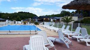 uma fila de cadeiras brancas junto a uma piscina em Bungalow de 3 chambres avec piscine partagee jardin et wifi a Louannec em Louannec