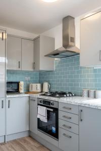 a kitchen with white cabinets and blue tiles at Stay at the Marine House - TV in every bedroom! in Morriston