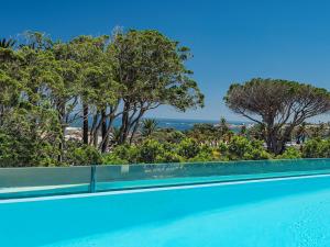 una piscina con árboles y el océano en el fondo en South Beach Camps Bay Boutique Hotel, en Ciudad del Cabo