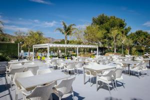 a patio with white tables and chairs and trees at Alannia Costa Dorada in Platja de l’Almadrava
