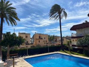 a swimming pool with a palm tree and some buildings at Escápate al Sol Apartamento con Piscina y Playa Cercana in Playa Pobla de Farnals