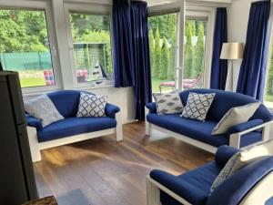 sala de estar con 2 sofás azules y ventanas en Ferienhaus Am See 19, en Zehdenick