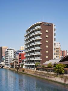 un edificio alto junto a un río con edificios en ALFACIO RIVERSIDE STAY HAKATA, en Fukuoka