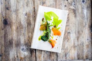 a white plate with vegetables on a wooden table at Trasti & Trine Boutique Hotel in Alta